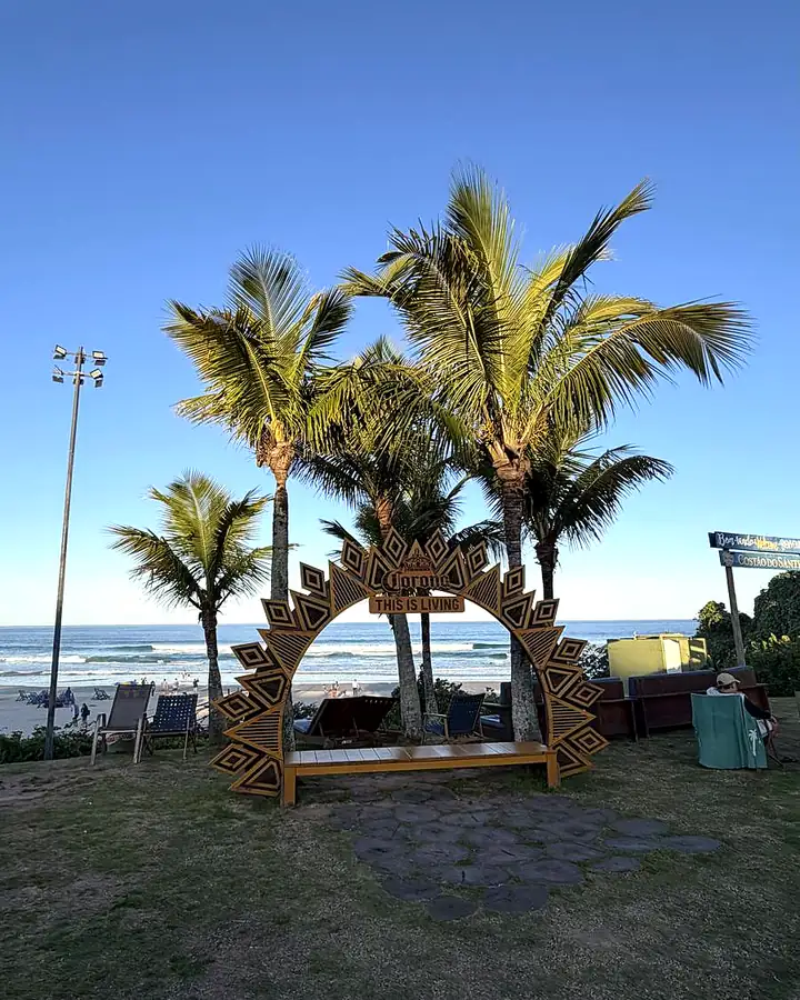 Arco de madeira com coqueiros e a praia ao fundo