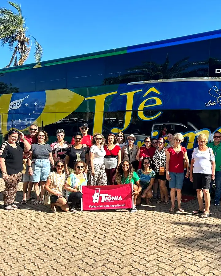 Grupo da Tiônia com a faixa da agência em frente ao ônibus de turismo