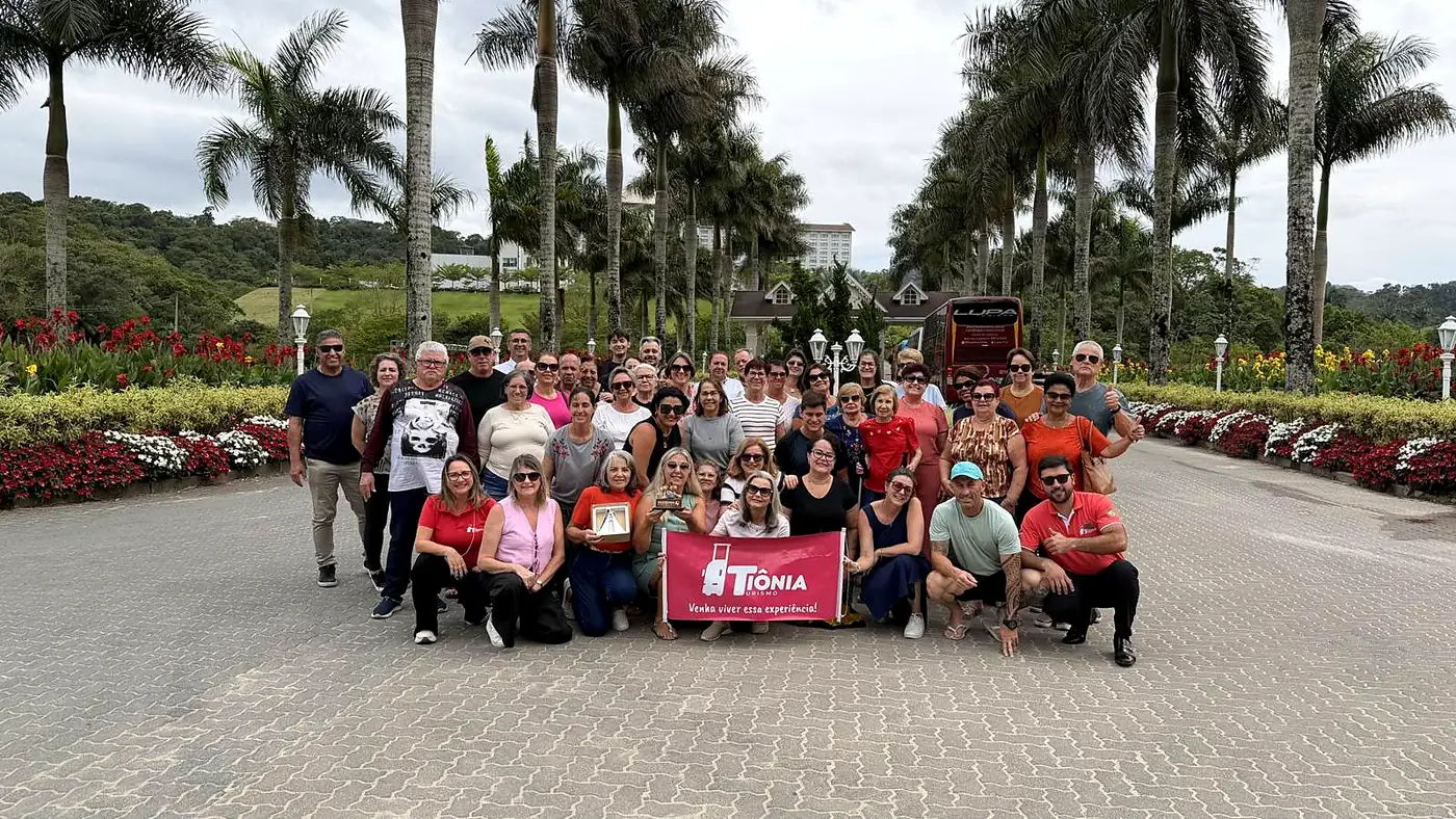 Grupo da Tiônia Turismo com a faixa da agência no jardim de palmeiras do Fazzenda Park Resort